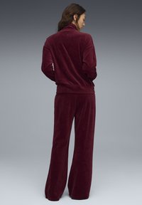 Burgundy corduroy tracksuit featuring a high collar jacket and wide-leg pants, both with ribbed texture and elastic cuffs.