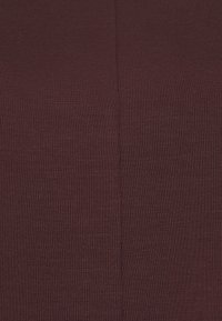 Close-up van donkerbruin ribbelstof met een centrale verticale naad, die textuur en stikdetails toont.