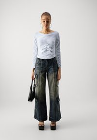 Lyseblå langermet topp med samlet detalj, kombinert med vide cargo-jeans med lommer og en falmet finish. Svart veske og plattformsko.