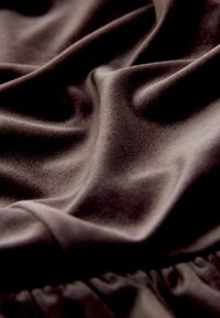Satenasta tkanina v čokoladno rjavi barvi z gladko, sijočo teksturo, z mehki gubami in nabranim robnim detajlom.