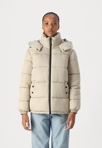 Beige pufferjakke med høy krage, glidelås foran, elastiske mansjetter og to svarte trykknapper på lommene. Glatt tekstur med horisontale sømmer.