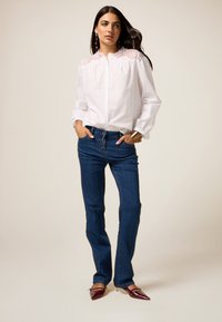 Cămașă albă cu nasturi, cu detalii din dantelă pe umeri, purtată cu blugi drepti de un albastru închis. Accente notabile din metal auriu pe blugi.