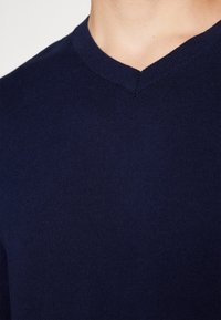 Mörkblå v-ringad tröja i mjukt, slätt tyg med figurnära passform och ribbad halskant. Sömmen vid kragen är synlig.