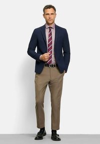 Navy blazer over a light purple shirt, paired with a striped maroon tie and beige trousers. Black shoes complete the look.