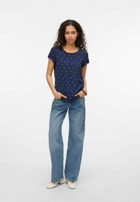 Marineblauw T-shirt met korte mouwen, versierd met groene en gele stippen, gecombineerd met wijduitlopende lichtblauwe jeans en crèmekleurige block-heel schoenen. Eenvoudig ontwerp, relaxte pasvorm.