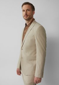 Beige colbert met een fijn gemêleerd patroon, notch-lapels, twee knopen en een enkel borstzakje, gecombineerd met een bruine blouse eronder.
