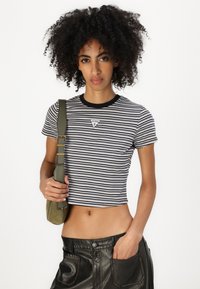 Stripet crop t-skjorte i svart og hvitt med rund hals og lite trekantet logo på brystet, kombinert med svarte skinnbukser med høy midje.