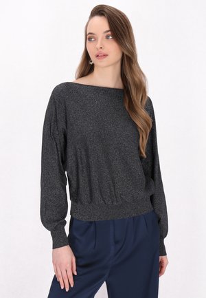 Schwarzer, glitzernder Pullover mit weitem Bootsausschnitt, langen Ballonärmeln und einem taillierten Saum, kombiniert mit dunkelblauen Hosen.