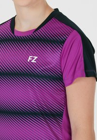 Lila träningsskjorta med svarta detaljer och diagonalt randmönster. Har rund hals och en vit "FZ"-logotyp på framsidan.