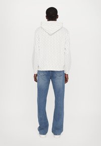 Vit hoodie med en strukturerad, upprepande mönster och en dragsko på huven, ihopparat med löst sittande blå denimjeans.