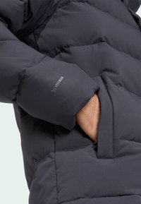 Tamnosiva jakna na prozračivanje s prošivenim uzorkom, s vidljivim džepom i diskretno brendiranim zakrpom na rukavu. Glatka tekstura i čvrsti materijal.