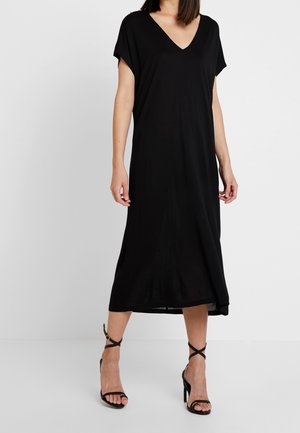 Czarna sukienka w serek z krótkimi rękawami, luźny krój, sięgająca do połowy łydki. Noszona z czarnymi sandałami na obcasie z paskami, gładka tekstura.