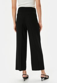 Zwarte wijde broek met hoge taille, gemaakt van gladde stof. Beschikt over twee achterzakken en een nette, op maat gemaakte afwerking.