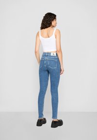 Blue skinny jeans with a high waist and subtle whiskering effect, paired with a white cropped tank top and black platform shoes.