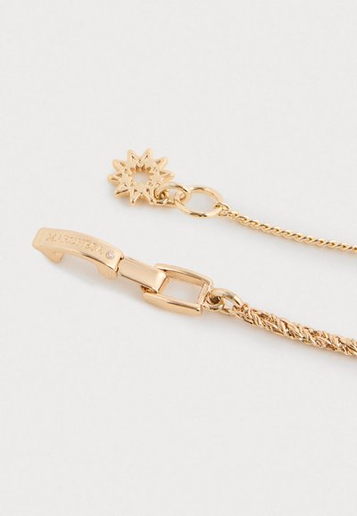 Chiusura di una collana in oro con inciso "MARCHESA" e un piccolo cristallo, attaccata a un ciondolo a forma di stella su sfondo bianco.