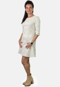 Vestido texturizado beige con mangas tres cuartos y dobladillo acampanado, combinado con botas de tobillo en tono marrón claro que cuentan con un tacón ancho.