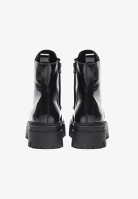 Bottines en cuir noir avec une semelle épaisse, des fermetures éclair sur le côté et des anses à l'arrière, dotées d'une finition lisse et brillante.
