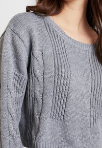 Szary sweter dziany z żebrowanymi i warkoczowymi splotami, z okrągłym dekoltem i luźnym krojem, podkreślający miękki, przytulny materiał.