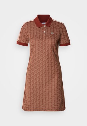 Brązowa sukienka typu polo z geometrycznym wzorem, krótkimi rękawami i kontrastującym kołnierzem. Posiada boczne paski oraz logo Lacoste na piersi.
