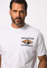 Hvid bomulds T-shirt med sort og orange bjerg-tema grafik og teksten "MOUNTAIN EXPERIENCE". Korte ærmer, rund halsudskæring.