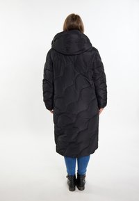 Sort puffjakke med hætte, med quiltede mønstre, lange ærmer og knæ-længde design. Bæres over blå jeans og sorte ankelstøvler.