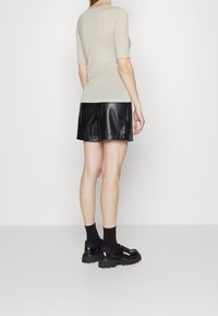 Jasnobeżowa dopasowana bluzka z krótkimi rękawami w połączeniu z czarną plisowaną spódnicą z ekologicznej skóry, uzupełniona masywnymi butami na platformie i czarnymi skarpetkami.