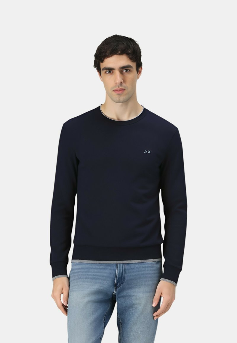 Marineblaues Sweatshirt aus glattem Stoff, mit Rundhalsausschnitt, gerippten Bündchen und einem dezenten Logo auf der Brust. Kombiniert mit hellblauen Jeans.