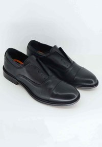 Scarpe in pelle nera con una finitura liscia, punta arrotondata, pannelli laterali elastici e dettagli di cucitura minimi. Suole piatte e design elegante.