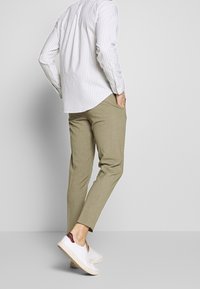 Lichtgrijze blouse met verticale strepen en lange mouwen, gedragen met khaki tapered broek en witte sneakers met een bordeauxrode accent op de hak.
