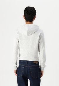 Grå hoodie med dragsko och mjuk textur, med ribbade ärmslut. I kombination med mörk denimjeans sedd bakifrån.