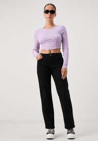 Light purple ribbed long-sleeve cropped top paired with black wide-leg trousers and black and white sneakers; model wearing sunglasses.