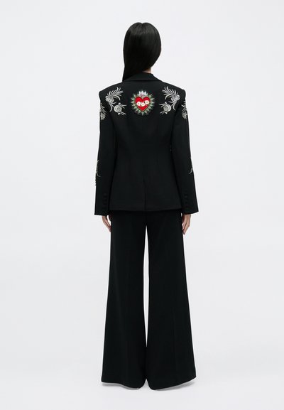 Fekete, testre szabott blézer virágos hímzéssel a vállakon és szívmintával a hátoldalon; széles szárú nadrággal párosítva. Sima textúra.