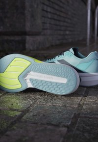 Des baskets légères de sport en bleu aqua avec une semelle texturée, présentant un accent jaune vif et le logo "LIGHTSTRIKE" sur la semelle intermédiaire.