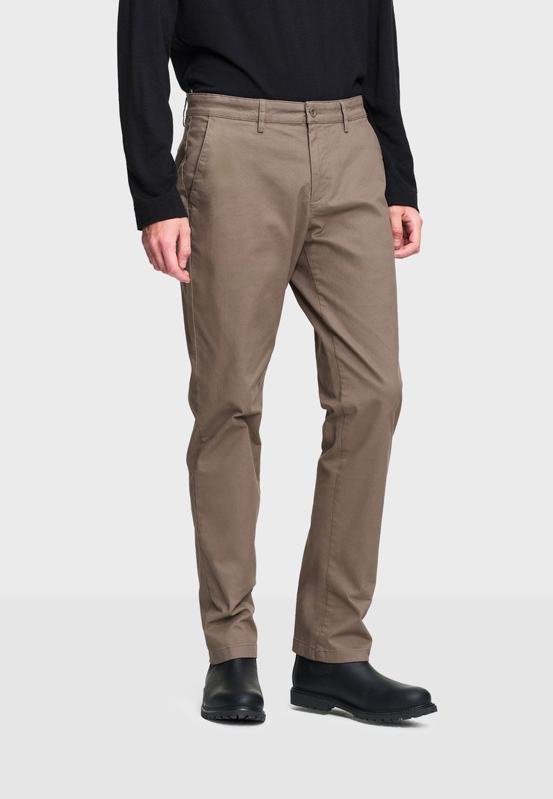 Beige chinos suora istuvuus, varustettuna nappikiinnityksellä ja vyölenkeillä, yhdistetty mustiin nilkkureihin. Sileä puuvillakangas.