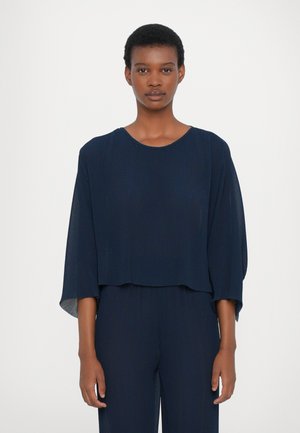 Marinblå cropped top med ribbet tekstur, brede ærmer og rund halsudskæring, parret med en matchende bund. Minimalistisk design.