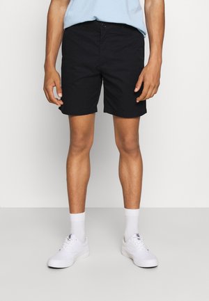 Schwarze Shorts aus Baumwollmischung, mit Knopfverschluss, seitlichen Taschen und geradem Schnitt, kombiniert mit weißen Sneakern und Socken.