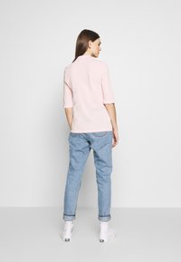 T-shirt rosa chiaro a girocollo e maniche a metà, abbinato a jeans azzurri a vita alta. Sneakers bianche con dettagli neri.