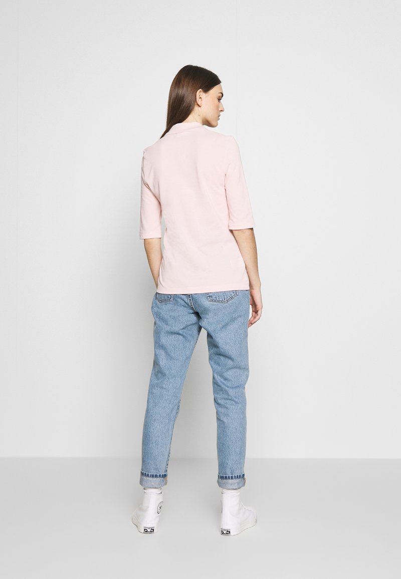 T-shirt rosa chiaro a girocollo e maniche a metà, abbinato a jeans azzurri a vita alta. Sneakers bianche con dettagli neri.