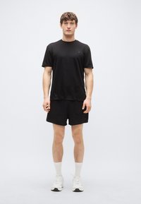 Svart atletisk t-shirt med korta ärmar, matchad med svarta shorts. Lätt, mjukt tyg med minimal branding. Vita strumpor och sneakers.
