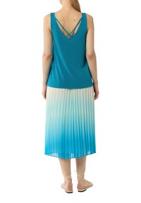 Niebieski bezrękawnik z dekoltem w kształcie litery V z krzyżującymi się ramiączkami, zestawiony z plisowaną spódnicą, która przechodzi od białego do niebieskiego.