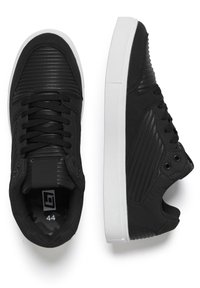 Schwarze Sneakers mit geripptem Synthetikobermaterial, strukturierten Akzenten, schwarzen Schnürsenkeln und weißer Gummisohle. Größe 44 im Inneren markiert.