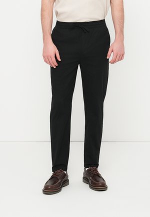 Pantaloni neri con cintura elastica e coulisse. Il materiale sembra liscio con un taglio a gamba dritta. Abbinati a scarpe marroni con lacci.