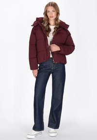 Bordeaux pufferjakke med aftagelig hætte, quiltet design, frontlukning med knapper og ribbede manchetter, parret med højhalset denim jeans og hvide sneakers.