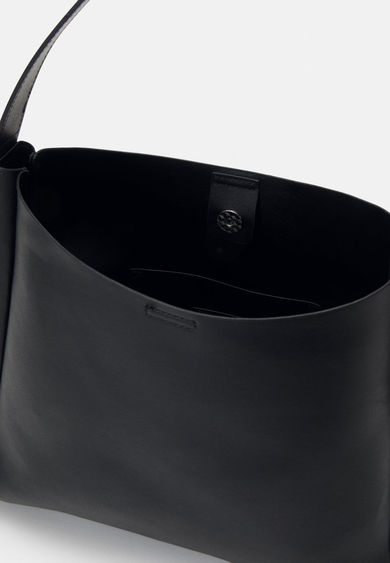 Borsa a mano in pelle nera con texture liscia, design aperto e tasca interna. Presenta una tracolla singola e dettagli con logo sulla patta.