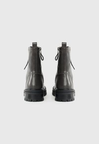 Bottines en cuir gris foncé avec une texture lisse, des tirettes, et une semelle en caoutchouc noir robuste avec un motif de semelle.