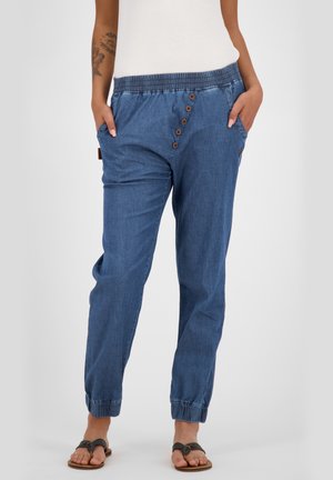 Pantalones jogger de mezclilla con cintura elástica, detalles en botón marrón, bolsillos laterales, puños ajustados y un corte relajado en un color azul intermedio.