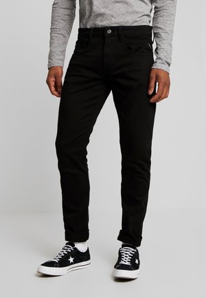 Jean en coton noir avec une coupe slim, dotés d'une fermeture à boutons, de poches avant et de ourlets roulés, associés à des baskets noires.