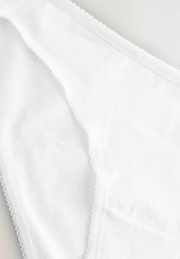Vita bomullsbikiniunderkläder med en mjuk textur, färdiga kanter och en delikat vågig kant, med en enkel design utan mönster.