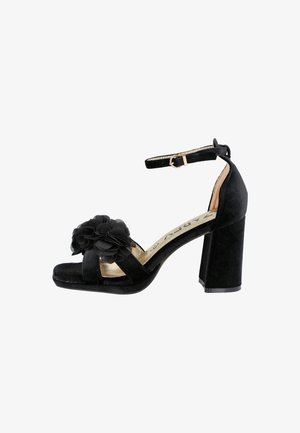 Sandalia de tacón alto de ante negro con correa en el tobillo, tacón cuadrado y adorno floral en capas en la correa delantera.