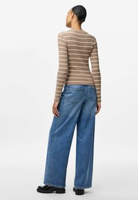 Brunrandig ribbad långärmad topp tillsammans med vida blå jeans och svarta platåskor, sedd bakifrån.